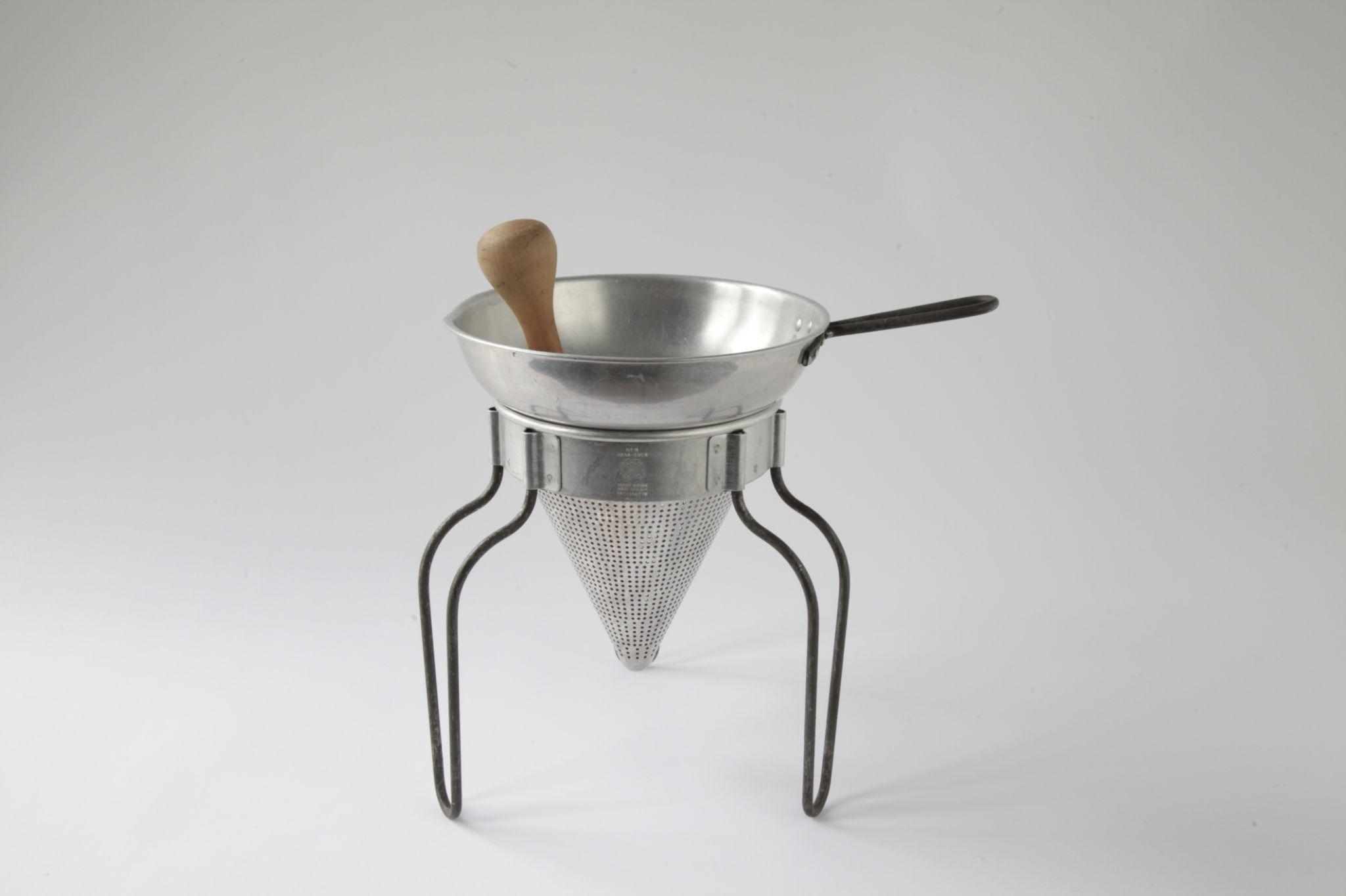 a metal sieve with a wooden handle in front of a neutral background.
